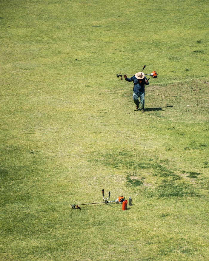Aerial view of a man in a hat working with grass trimmer in a sunny field.