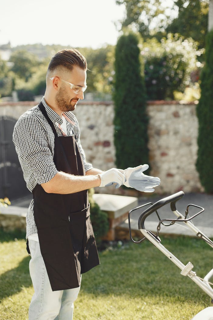 A man in gloves and apron prepares to mow the lawn on a sunny day.